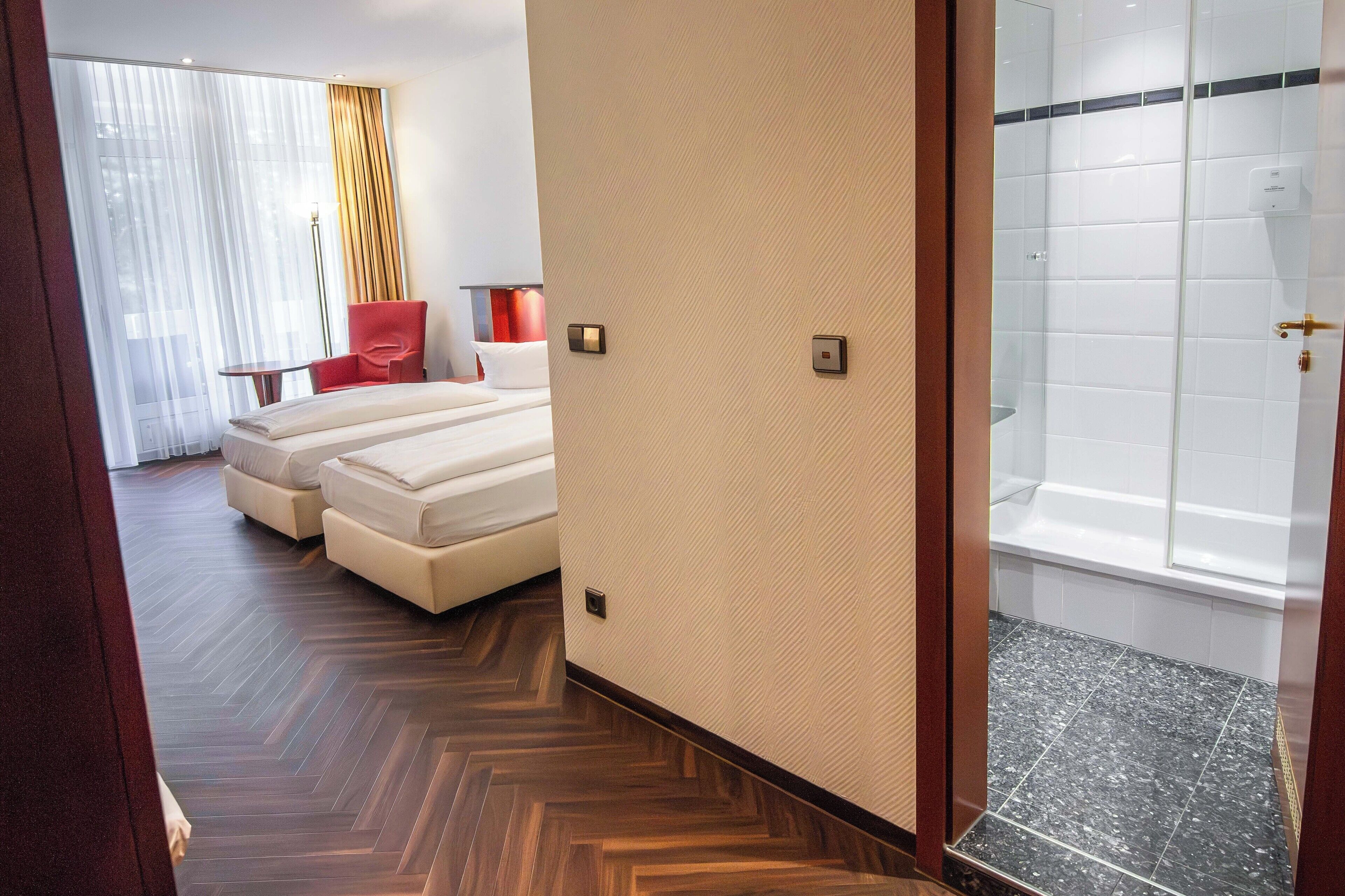A hotel room with a large bed, a separate sofa, a small table, and a shower area.