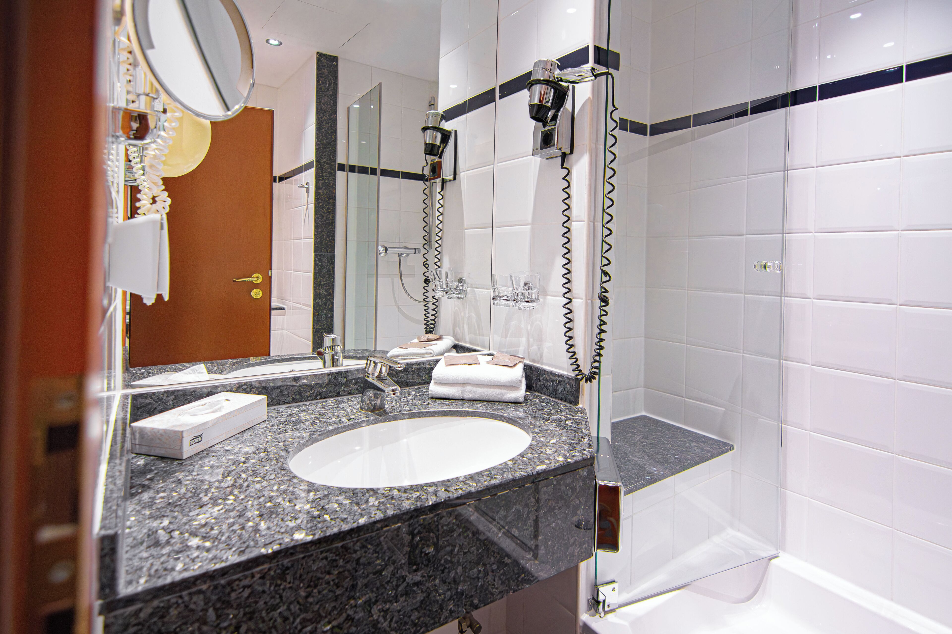 A bathroom with a granite countertop, a white sink, a mirror, and a shower area.