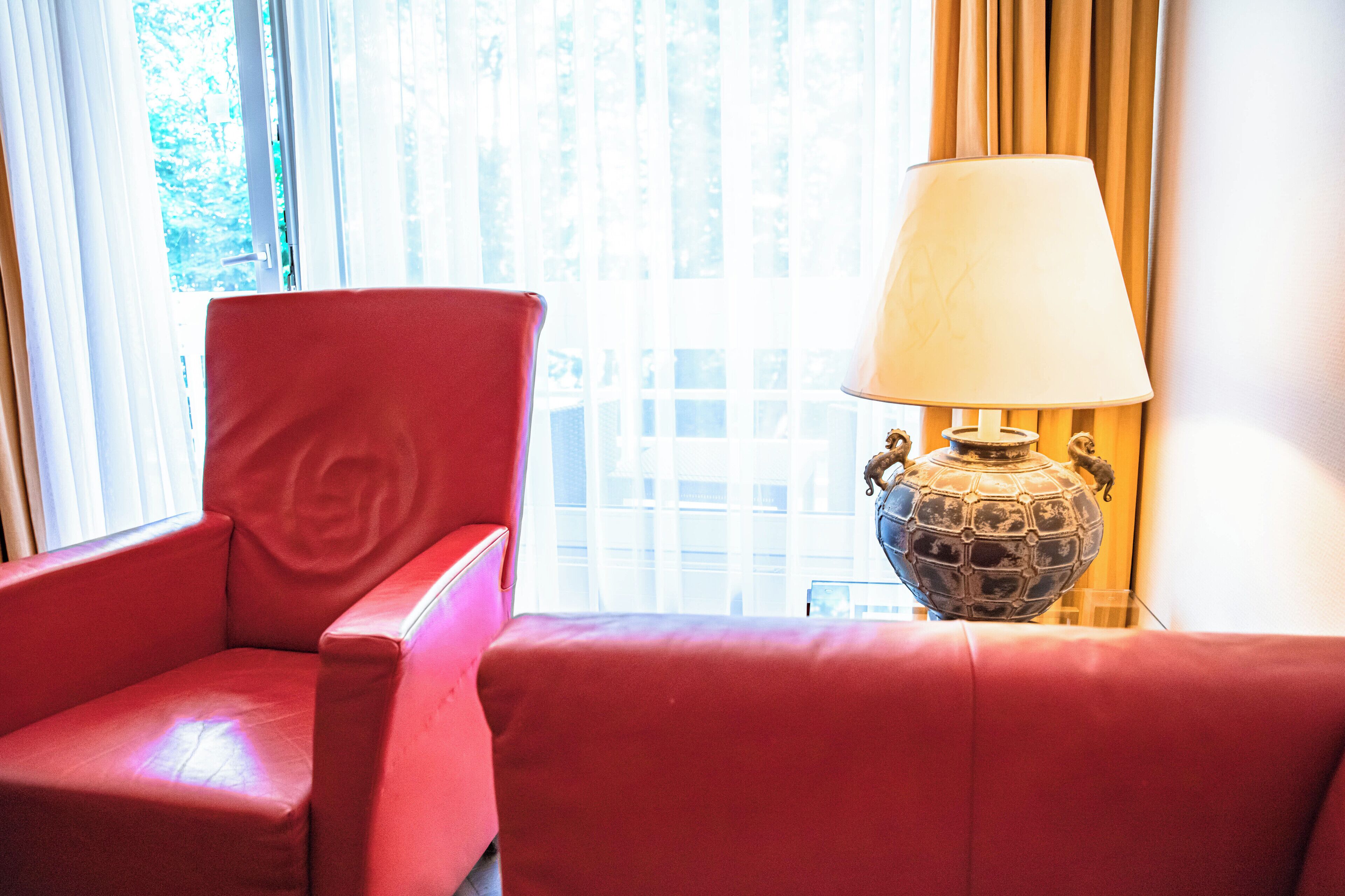 A red leather chair and a table lamp with a globe base in a room with a window and curtains.