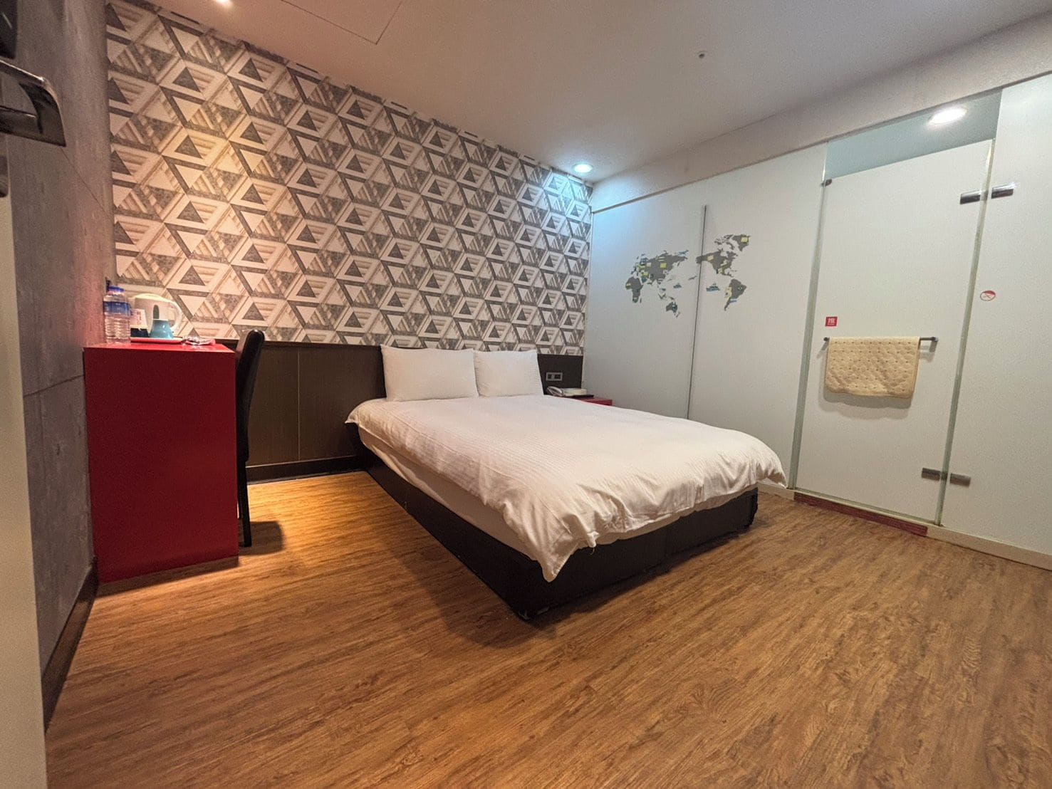 A hotel room with a bed, a wardrobe, a desk, and a patterned wall.