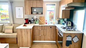 A modern kitchen with wooden cabinets, a built-in stove, and a countertop with various appliances. - Mobil Home (ST-GEORGES-DOLERON)