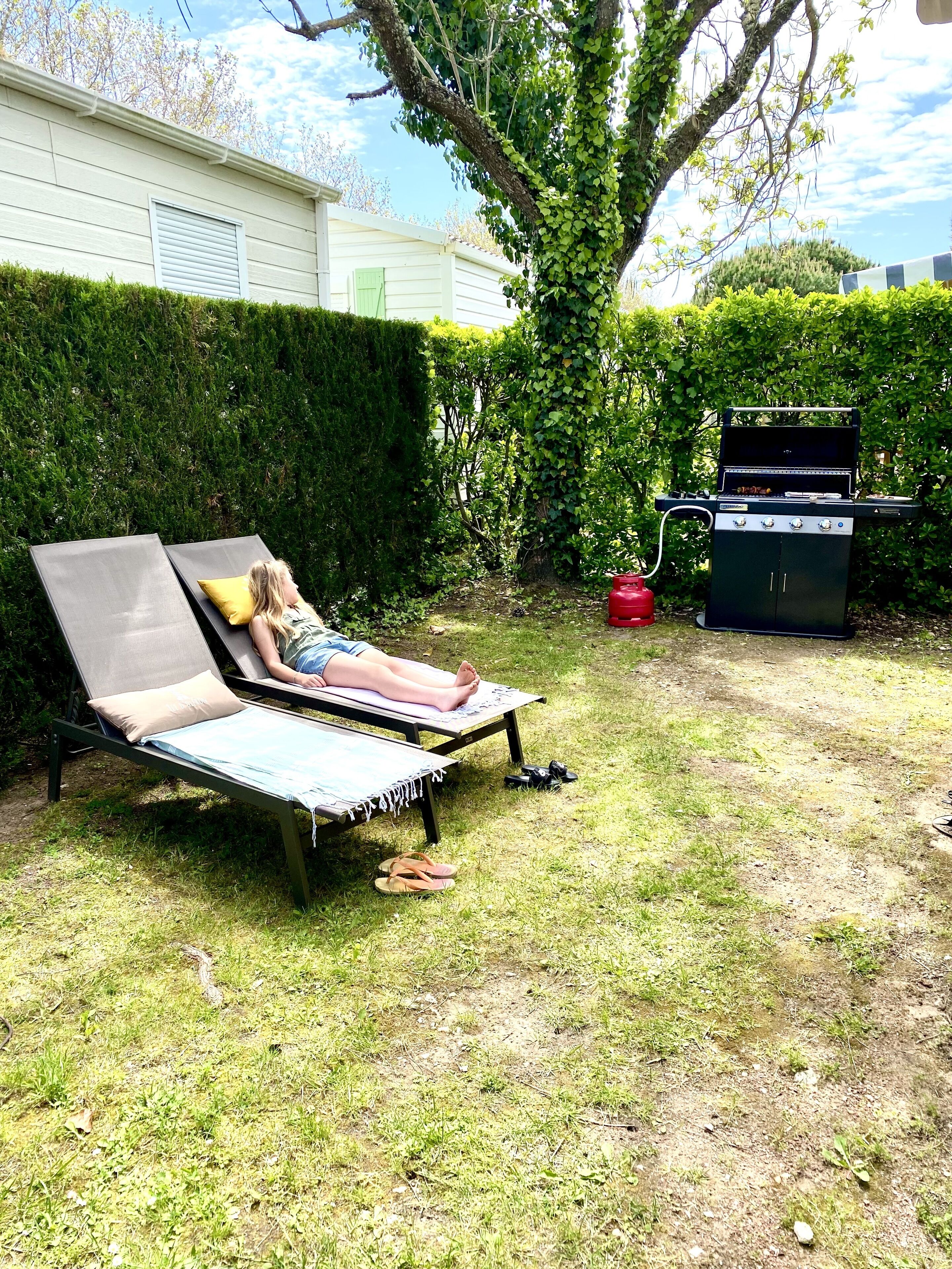 Un jardin avec un fauteuil de relaxation, un barbecue et une haie.