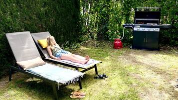 Un jardin avec un fauteuil de relaxation, un barbecue et une haie.