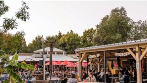 Restaurante al aire libre con mesas y sombrillas rojas, rodeado de árboles.