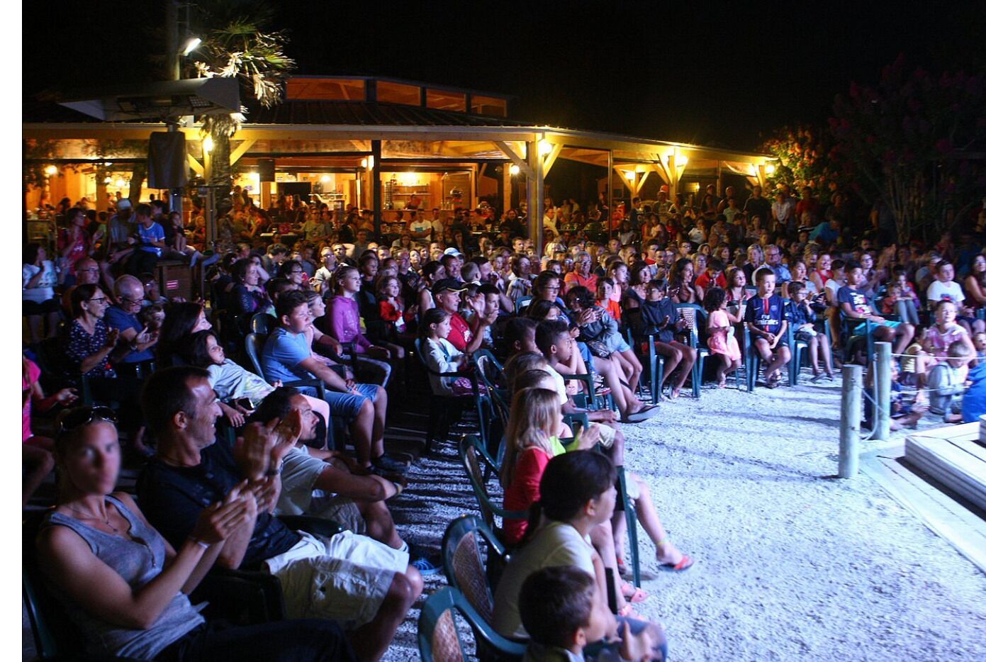 An outdoor seating area with people seated on chairs, facing a stage or performance area.