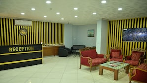 A reception area with a reception desk, seating area with red upholstered chairs, a coffee table, and a wall-mounted television. - Elite Holiday Hotel (Trabzon)