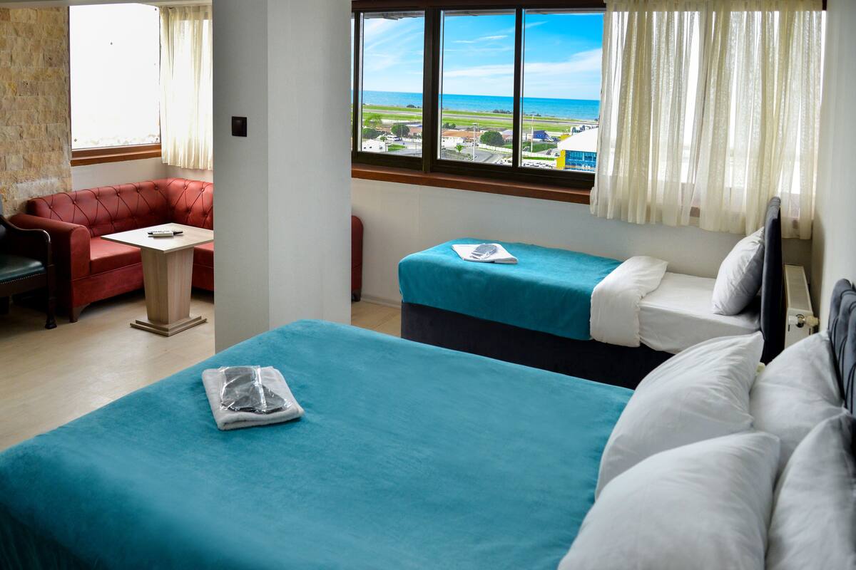 A hotel room with two beds, a red sofa, a small table, and a window with a view of the beach and ocean.