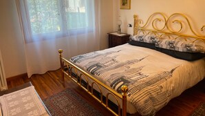 A bedroom with a bed, a nightstand, a chandelier, and a window with curtains.