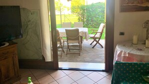 An open door leading to a patio with a table and chairs, a television in the room, and a painting on the wall.