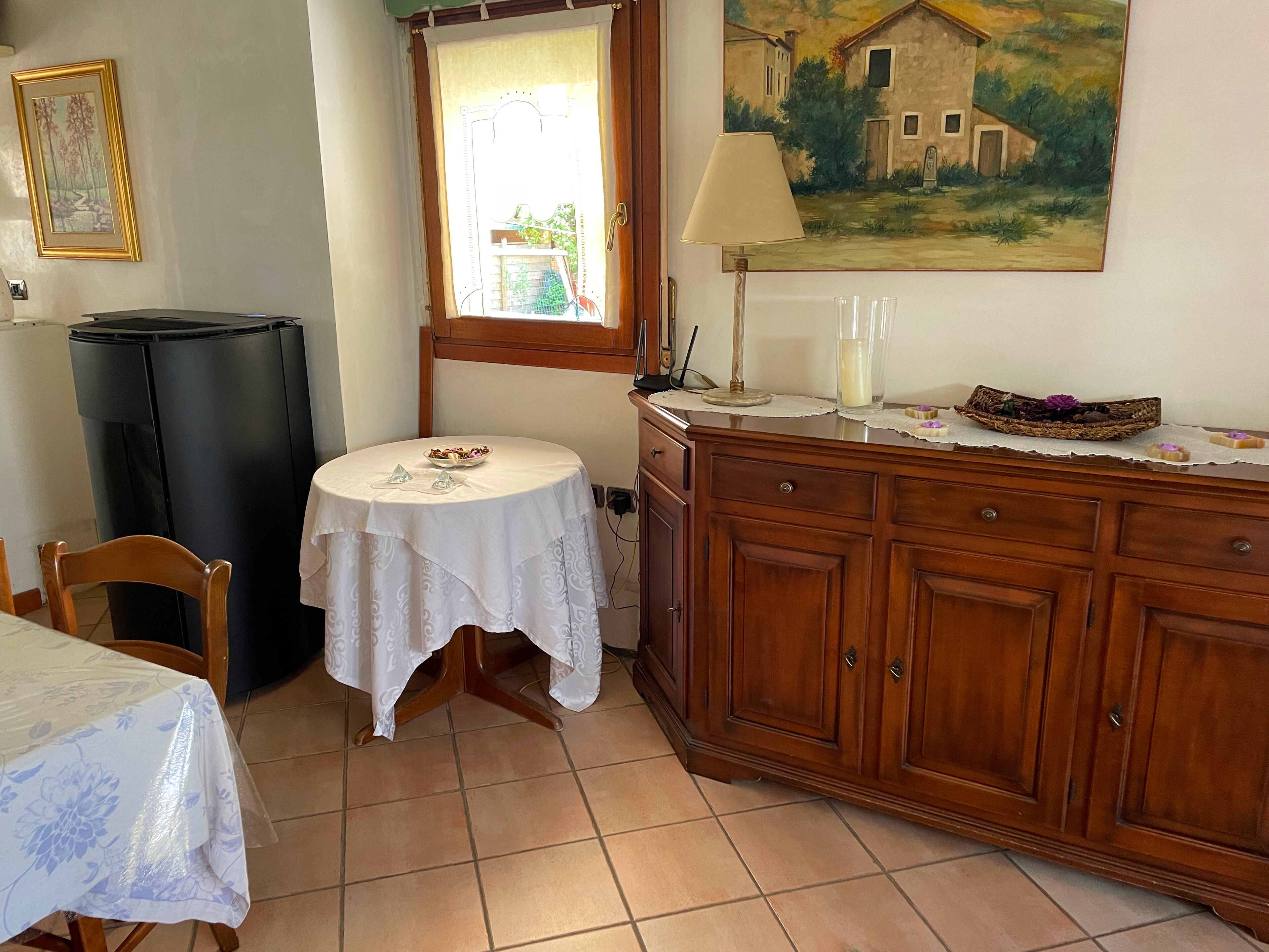 A dining area with a round table, chairs, a black refrigerator, a wooden cabinet, and a painting on the wall.