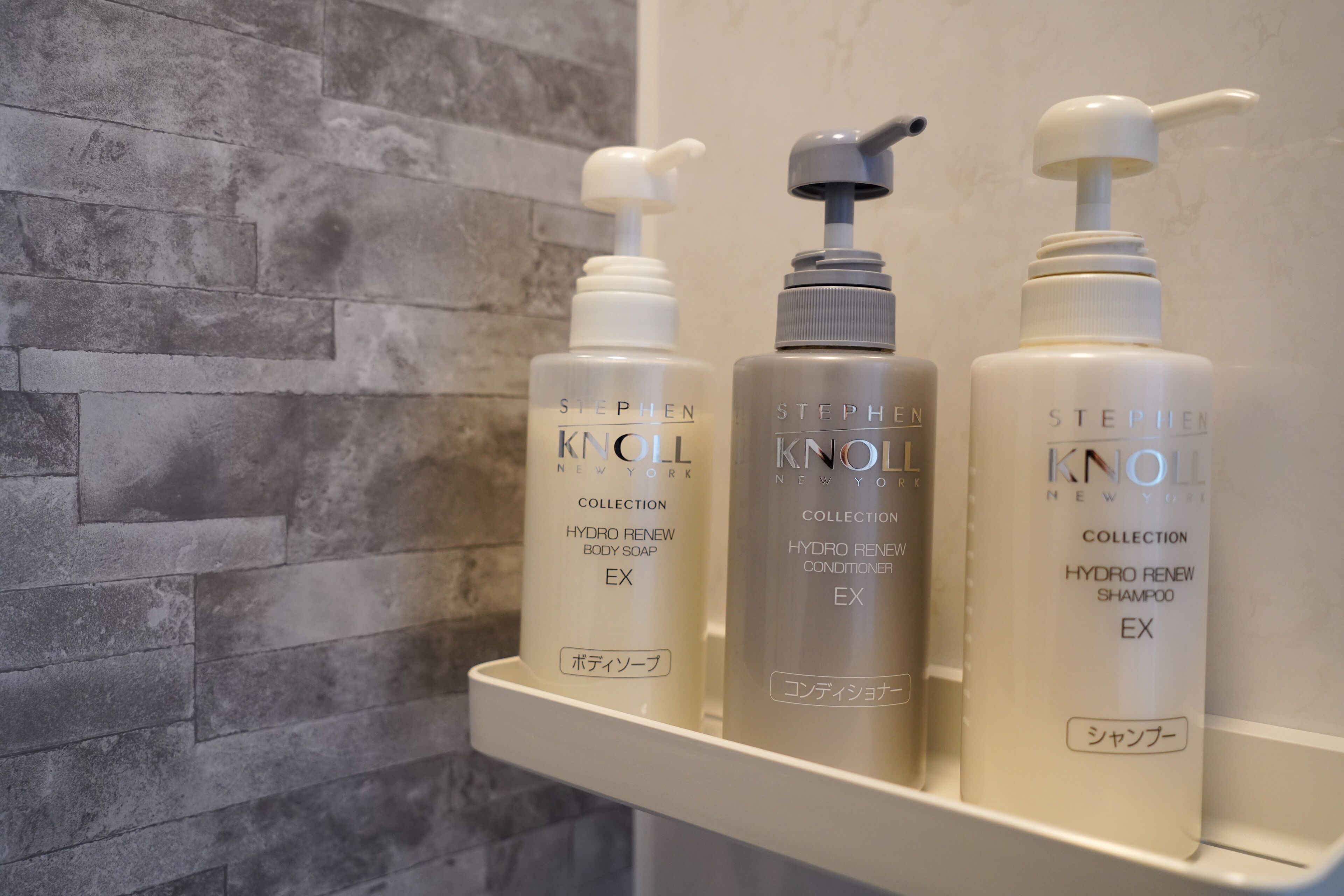 Un estante de baño con tres productos de Stephen Knoll Collection: jabón corporal, acondicionador y champú.