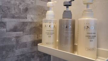Un estante de baño con tres productos de Stephen Knoll Collection: jabón corporal, acondicionador y champú.