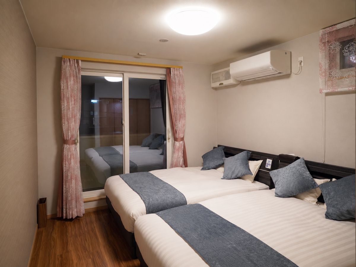 A hotel room with two beds, a sliding door to a balcony, and an air conditioning unit on the wall.