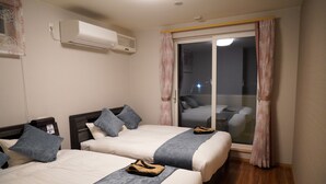 A hotel room with two beds, a sliding glass door to the balcony, and an air conditioning unit on the wall. - Hakodate MOTOMACHI  guesthouse (Hakodate)