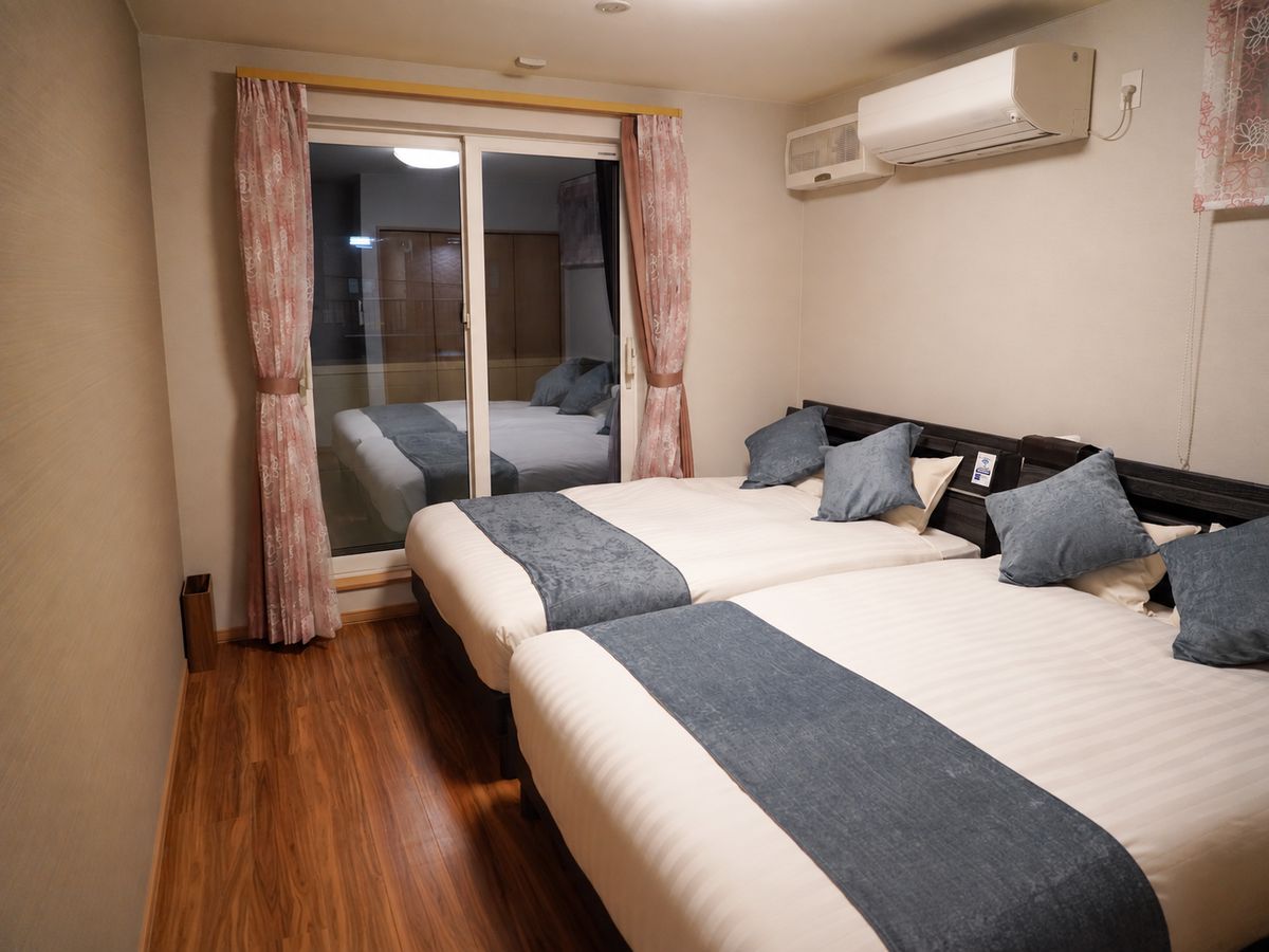 Ein Hotelzimmer mit zwei Betten, einer Schiebetür, einer Klimaanlage und Holzboden.