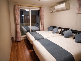 Habitación de hotel con dos camas, una puerta corrediza de vidrio, un equipo de aire acondicionado y piso de madera.