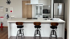 A modern kitchen with a central island, bar stools, a built-in oven, and a stainless steel refrigerator. - Hakodate MOTOMACHI  guesthouse (Hakodate)