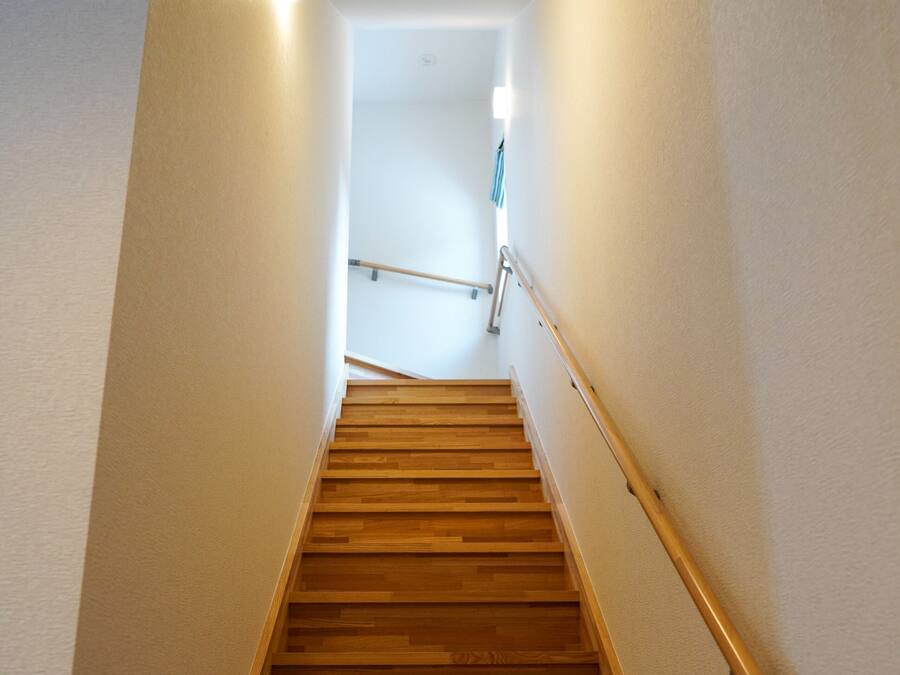 A wooden staircase with a handrail, leading to a landing with a light fixture.