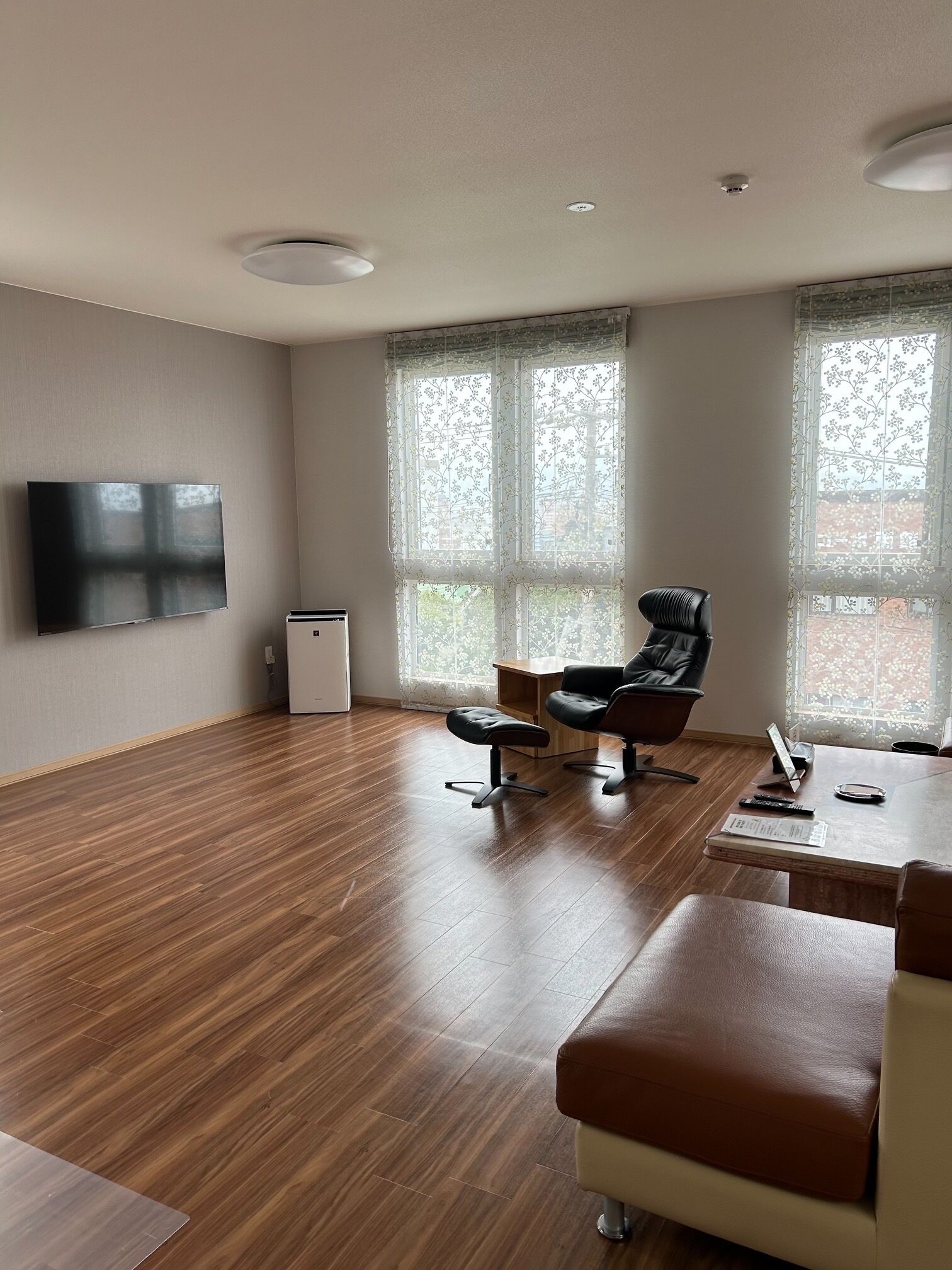 Un salón espacioso con televisor de pantalla plana, un sillón de cuero negro, una mesa de centro de madera y un refrigerador blanco pequeño.