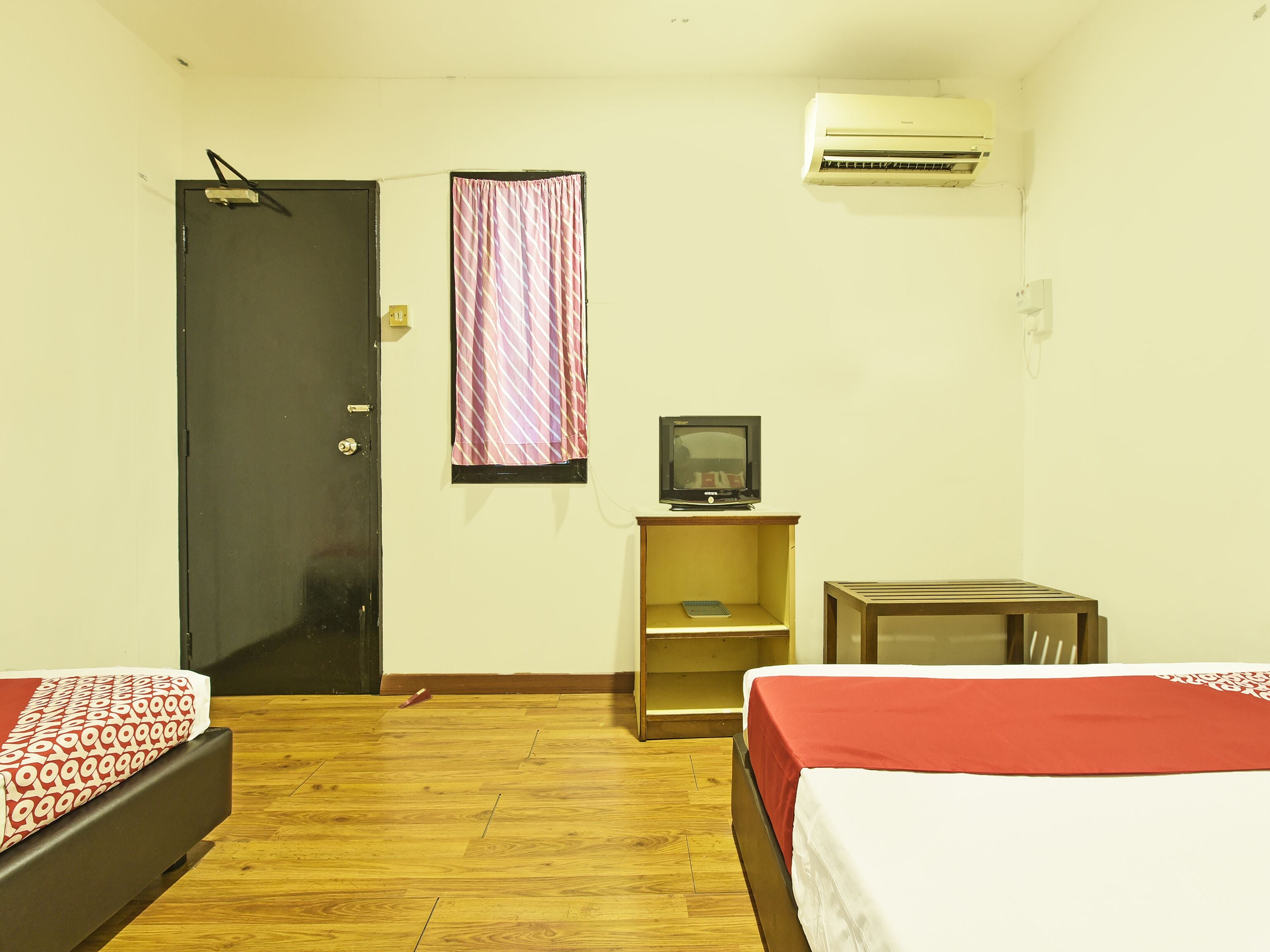 A hotel room with two beds, a television, an air conditioner, and a door.