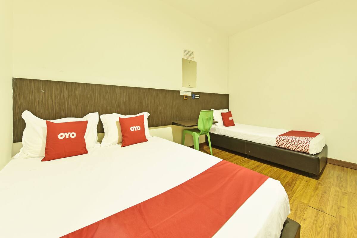 Habitación de hotel con dos camas, cada una con ropa de cama blanca y roja, una silla verde y suelo de madera.