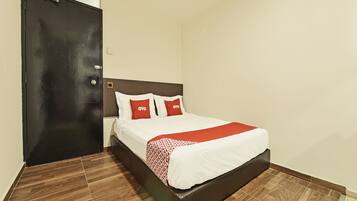 A hotel room with a wooden floor, a bed with white bedding and red pillows, and a black door.