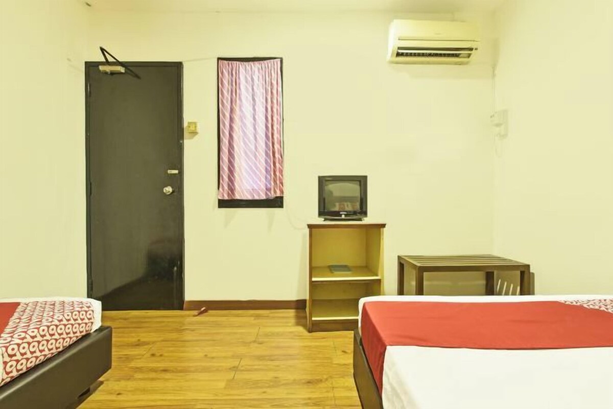 Una habitación pequeña y sencilla con cama, escritorio, silla, televisor y aire acondicionado.