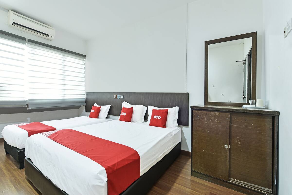 Una habitación de hotel con una cama grande, dos mesitas de noche, un armario y una ventana con persianas.