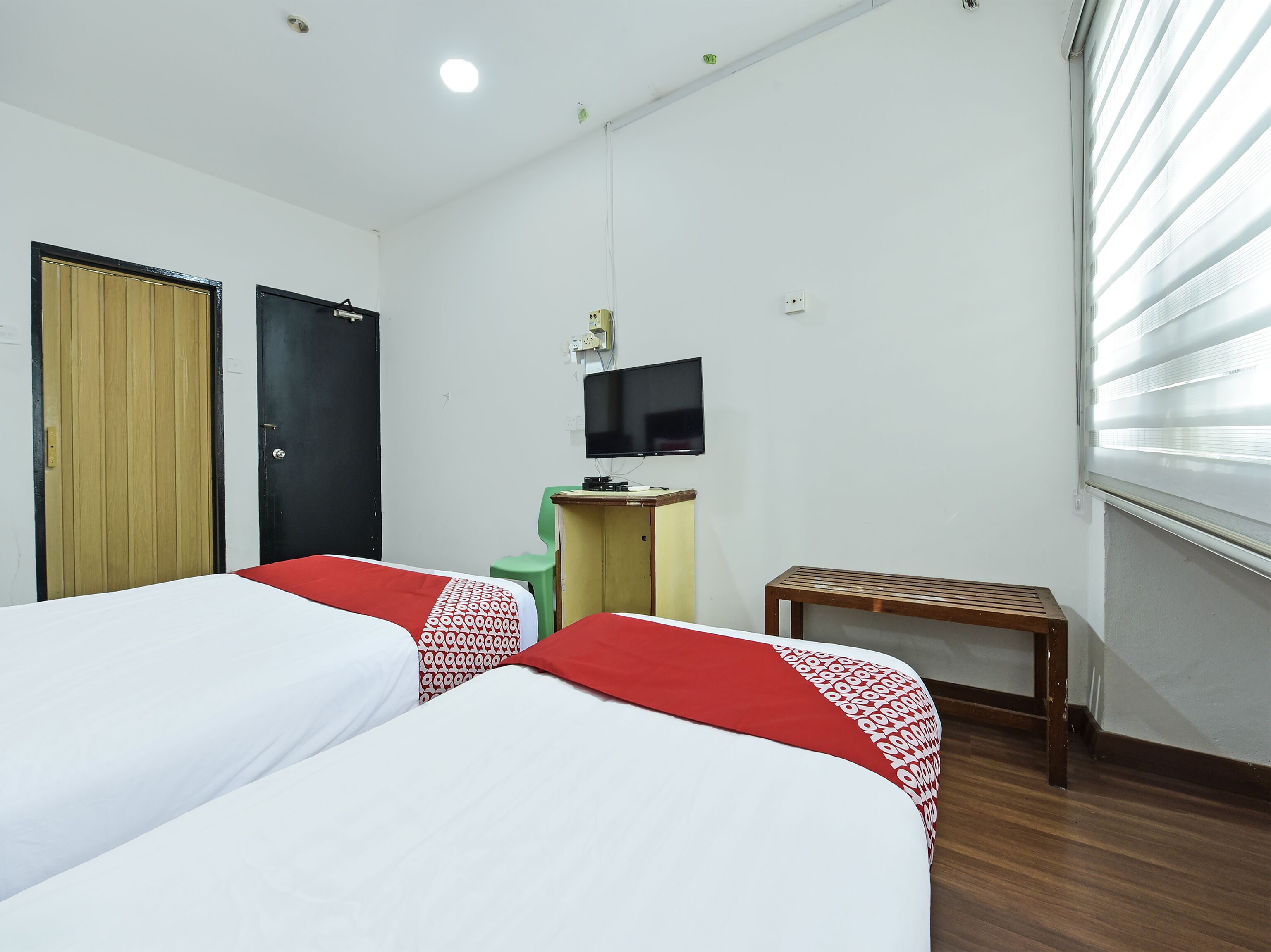 A hotel room with two beds, a television, a desk, and a window with blinds.