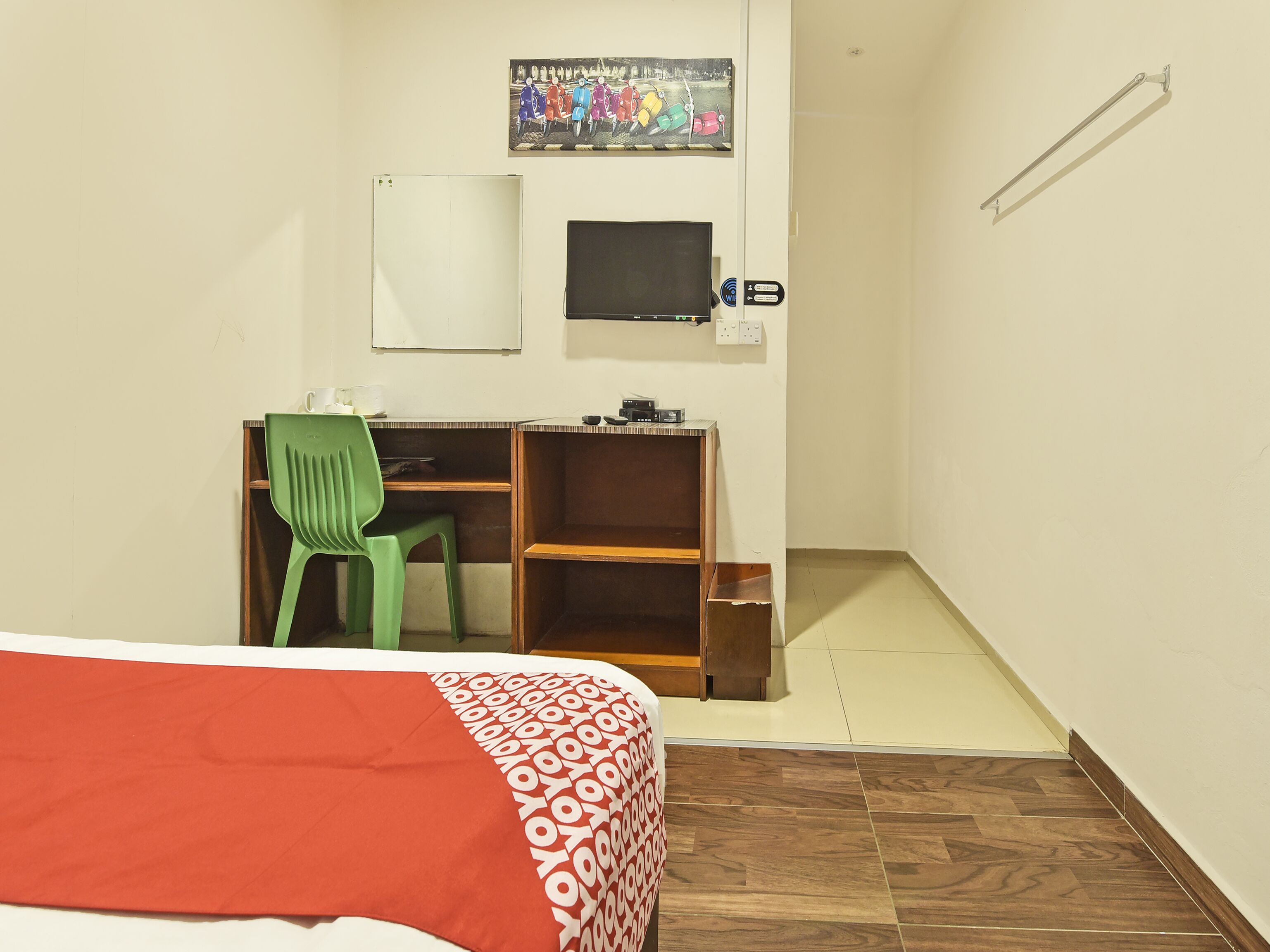 Una habitación pequeña y ordenada con una cama, un escritorio, una silla, un televisor y un cartel en la pared.