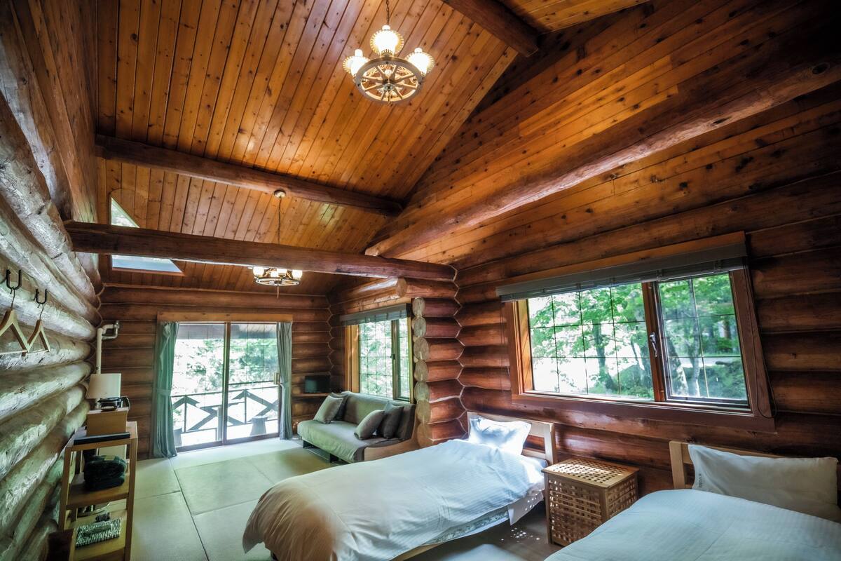 Een slaapkamer in een blokhut met twee bedden, een kroonluchter en grote ramen.
