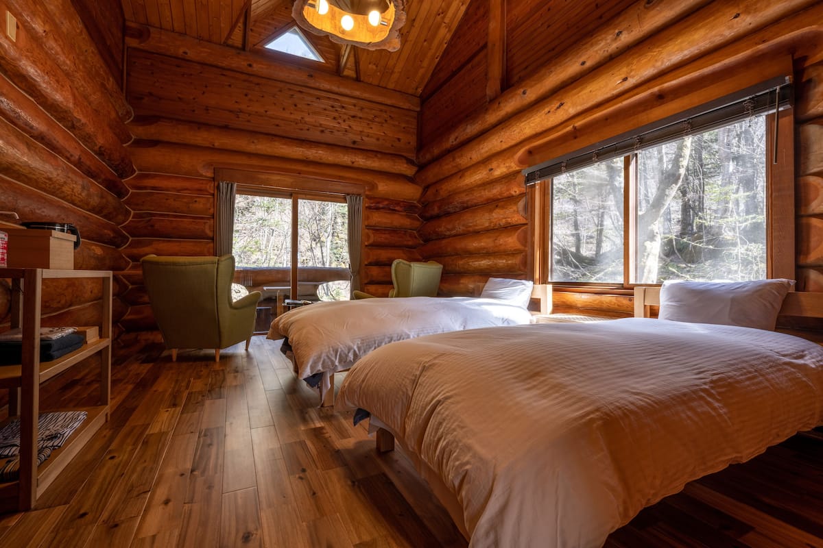 Een slaapkamer in een blokhut met twee bedden, een boekenplank en grote ramen.