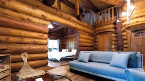Ein Holzblockhaus-Interieur mit einer Couch, einem gewebten Pouf und einem Holztisch.