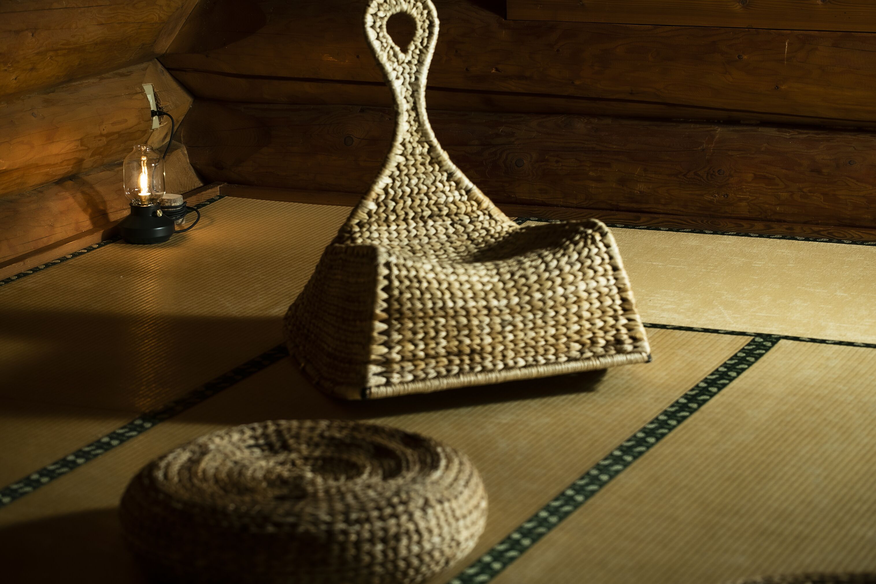A woven basket on a tatami mat with a glass bottle and a candle holder in the background.