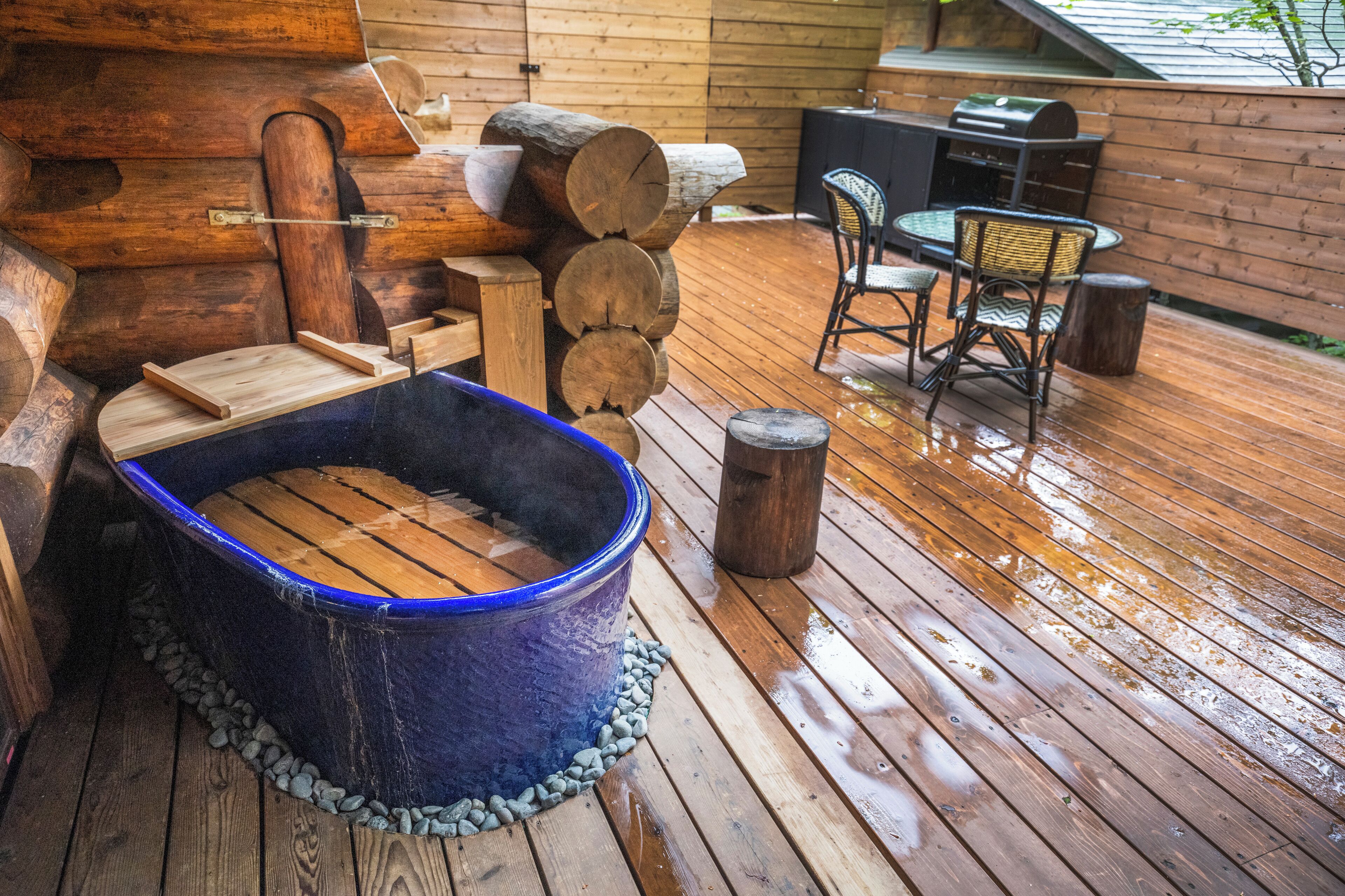 Una terrassa de fusta amb un bany d'hidromassatge, una barbacoa i mobles d'exterior.