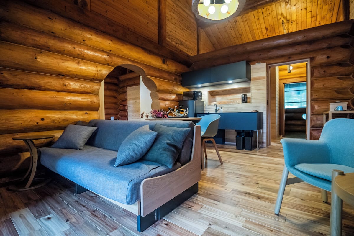 Een chaletinterieur met een bank, stoelen, een kleine tafel en een keukenhoek.