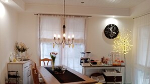 A dining area with a wooden table and chairs, a chandelier, a clock, and a decorative light on the wall. - Kőszeghegyalja Vendégház (Horvátzsidány)