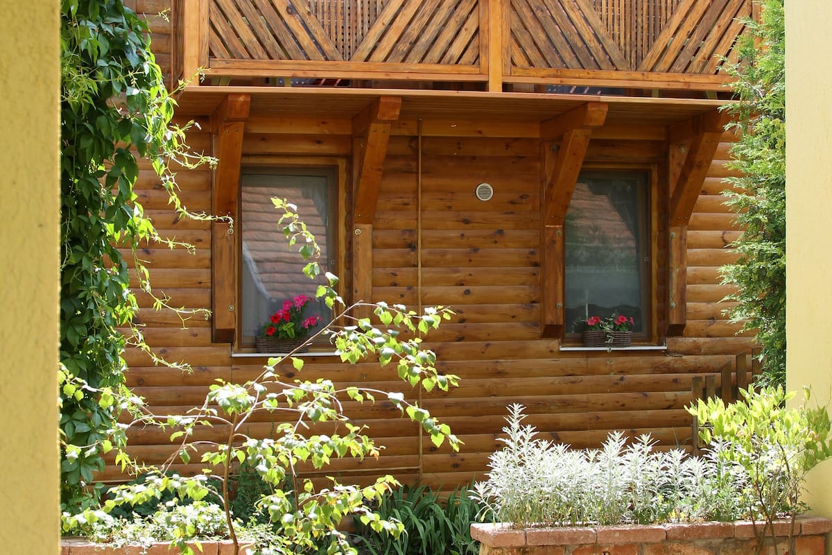 A wooden cabin with a balcony, windows, and a brick planter with plants.