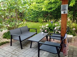 Ein Sitzbereich im Freien mit Tisch und zwei Stühlen, umgeben von üppiger Bepflanzung und blühenden Pflanzen.