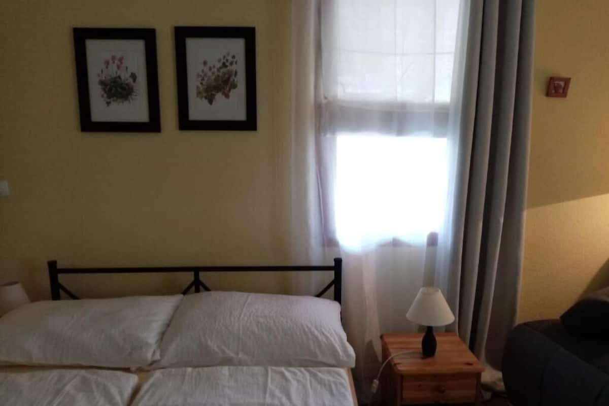 A room with a bed, a nightstand, a lamp, and two framed pictures on the wall.