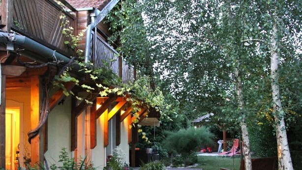 A wooden house with a covered porch and a brick pathway leading to a bench. - Kőszeghegyalja Vendégház (Horvátzsidány)