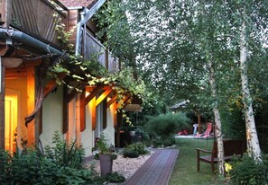 A wooden house with a covered porch and a brick pathway leading to a bench. - Kőszeghegyalja Vendégház (Horvátzsidány)