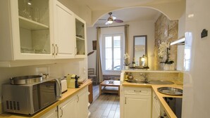 Een kleine keuken met witte kasten, een magnetron, een spoelbak en een eethoek met een tafel en stoelen.
