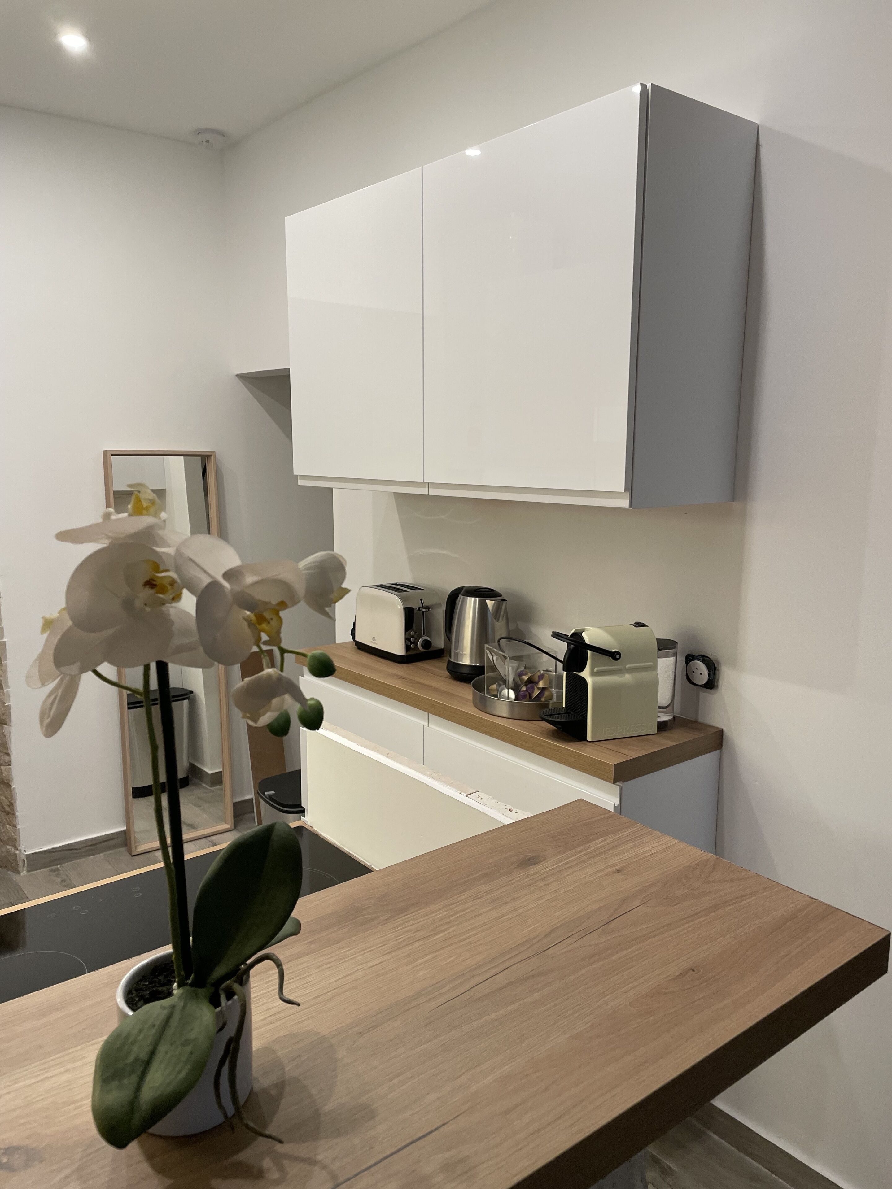 Une cuisine moderne avec des meubles blancs, un plan de travail en bois, un grille-pain, une bouilloire et une machine à café.
