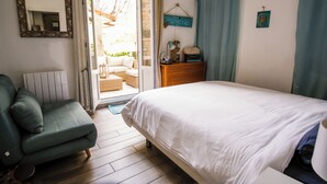 Een slaapkamer met een bed, een stoel, een dressoir en een raam met gordijnen.