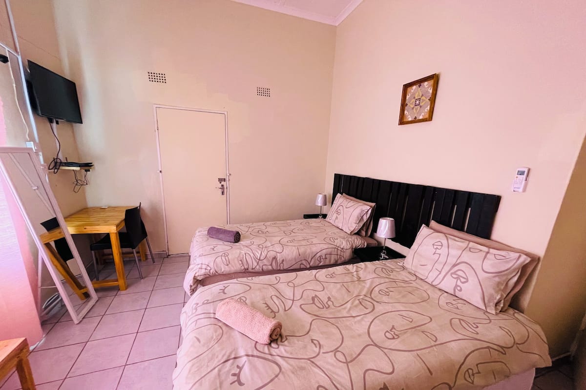 Una habitación con dos camas, un escritorio y un televisor montado en la pared.