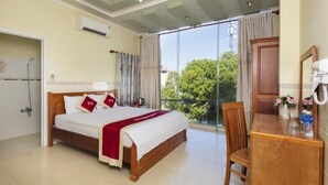 Habitación de hotel con cama, escritorio y vistas a árboles a través de amplias ventanas.