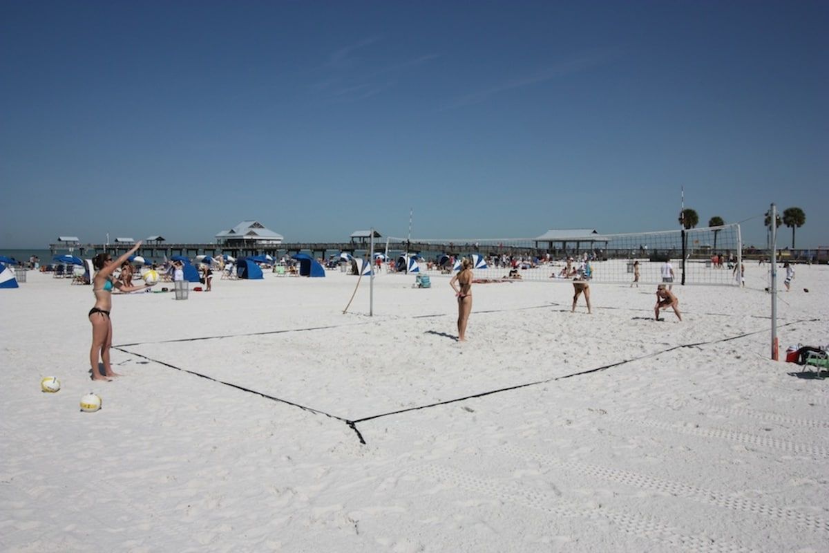Een strandvolleybalveld met spelers, strandparasols en strandhutten op de achtergrond.