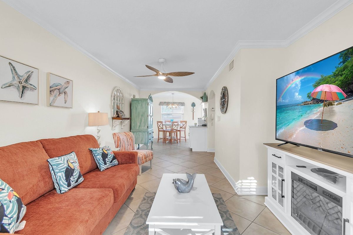 A living room with a sofa, coffee table, and a television displaying a beach scene.