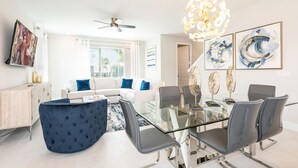 Ein modernes Wohnzimmer mit einem Glastisch, grauen Stühlen, einem weißen Sofa und einem Deckenventilator.